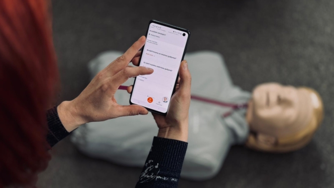 Sieviete rokās tur telefonu un uz grīdas redzams manekens