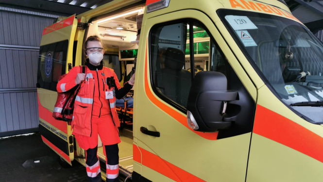 Mediķe NMPD formā un ar respiratoru, ar somu plecā stāv pie operatīvā auto