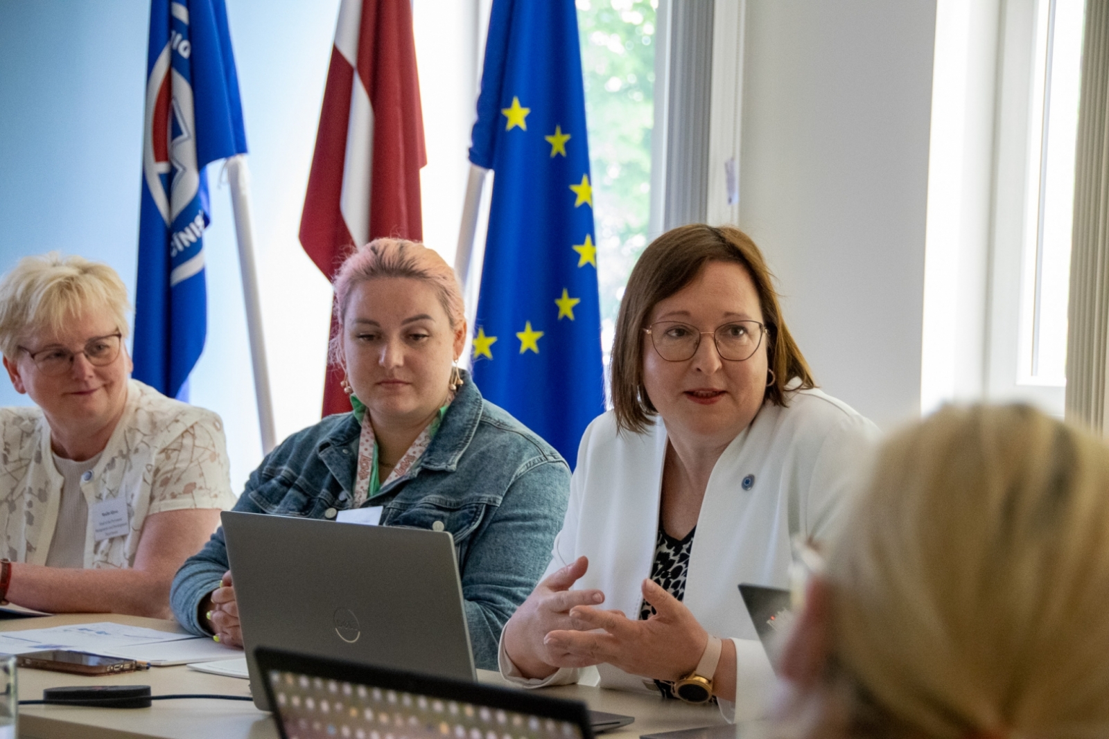 NMPD direktore runā ar klātesošajiem. Fonā karogi