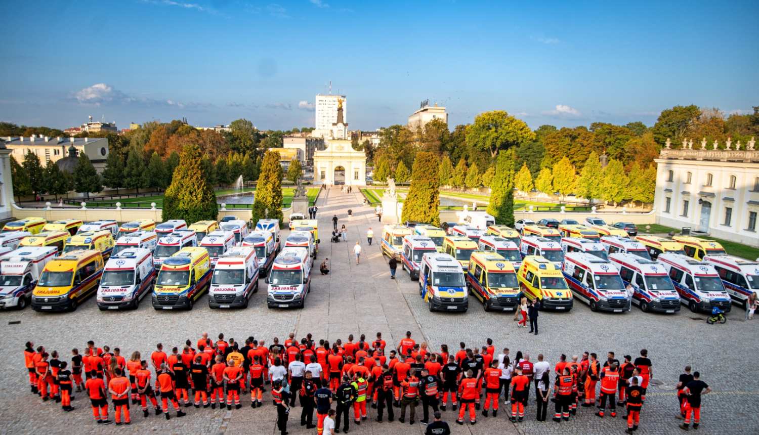 Skats no augšas, kur redzamas daudz dažādu ārvalstu ambulances un priekšā stāv daudz mediķu un paramediķu oranžās formās