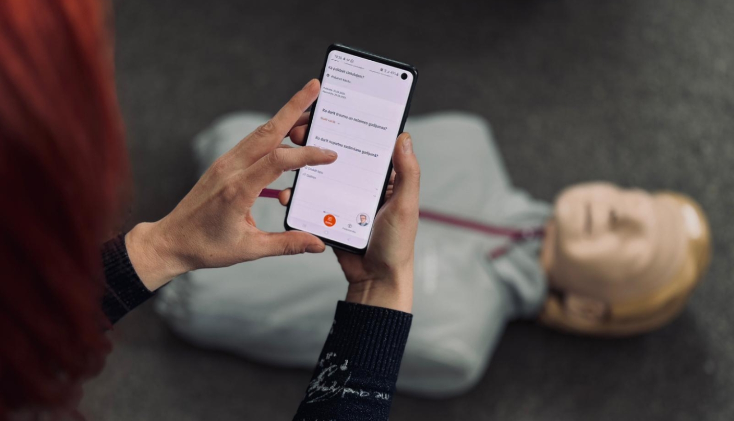 Sieviete rokās tur telefonu un uz grīdas redzams manekens
