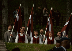 Cilvēki tautas tērpos tur rokās Latvijas karogus
