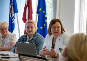 NMPD direktore runā ar klātesošajiem. Fonā karogi