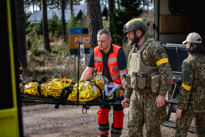 NMPD mediķis mācībās operatīvajā auto ievieto uz nestuvēm esošu cietušo. Blakus NBS pārstāvji formās