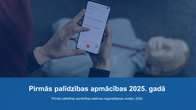 Pirmās palīdzības apmācības 2025. gadā. Manekens uz grīdas un cilvēks tur rokās telefonu