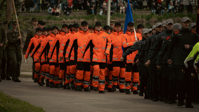 NMPD darbinieki oranžās formās soļo militārajā parādē