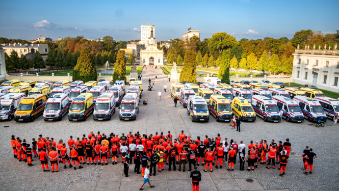 Skats no augšas, kur redzamas daudz dažādu ārvalstu ambulances un priekšā stāv daudz mediķu un paramediķu oranžās formās