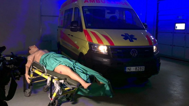 Manekens uz nestuvēm, fonā operatīvais auto ar ieslēgtām signālugunīm