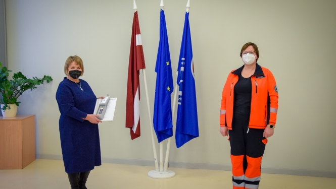 Stella Lapiņa ar NMPD direktori stāv pie valsts un dienesta karogiem