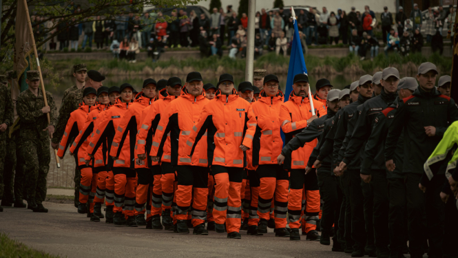 NMPD darbinieki oranžās formās soļo militārajā parādē