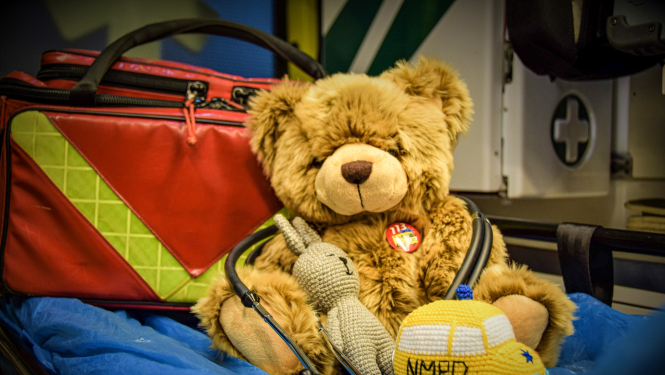 Rotaļu lācītis uz nestuvēm un tamborētu operatīvo medicīnisko auto