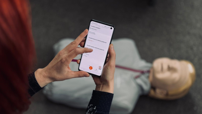 Sieviete rokās tur telefonu un uz grīdas redzams manekens