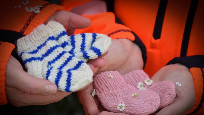 Divi mediķi rokās tur adītas zīdaiņu zeķītes rozā un zili/baltā krāsā