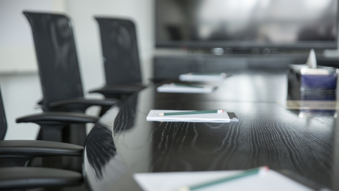 Tumšs biroja galds uz kura stāv lapiņas ar pildspalvām