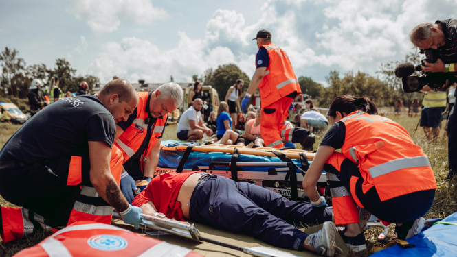 NMPD mediķi mācībās sniedz palīdzību. Apkārt 4 mediķi oranžās formās, priekšplānā soma