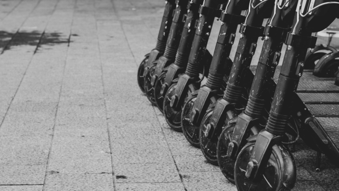 vairāki elektroskrejriteņi nolikti uz ielas, redzama priekšējā riteņa daļa