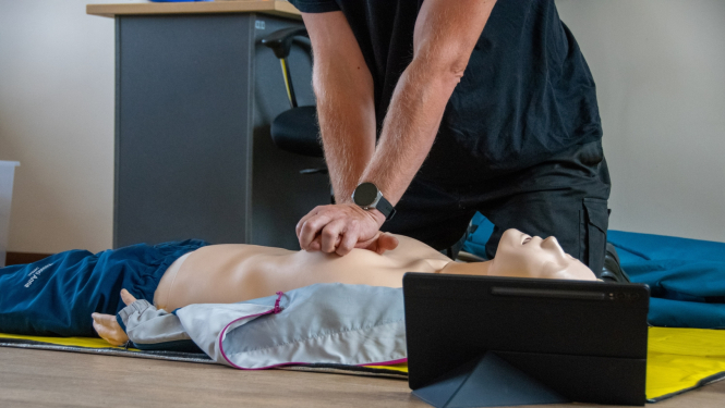 uz manekena sniedz atdzīvināšanas pasākumus. Manekenam blakus stāv planšetdators