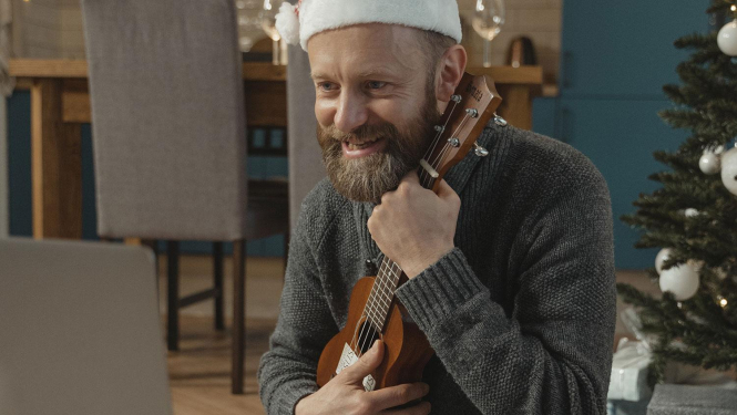 Vīrietis ar rūķu cepuri galvā spēlē ukuleli 