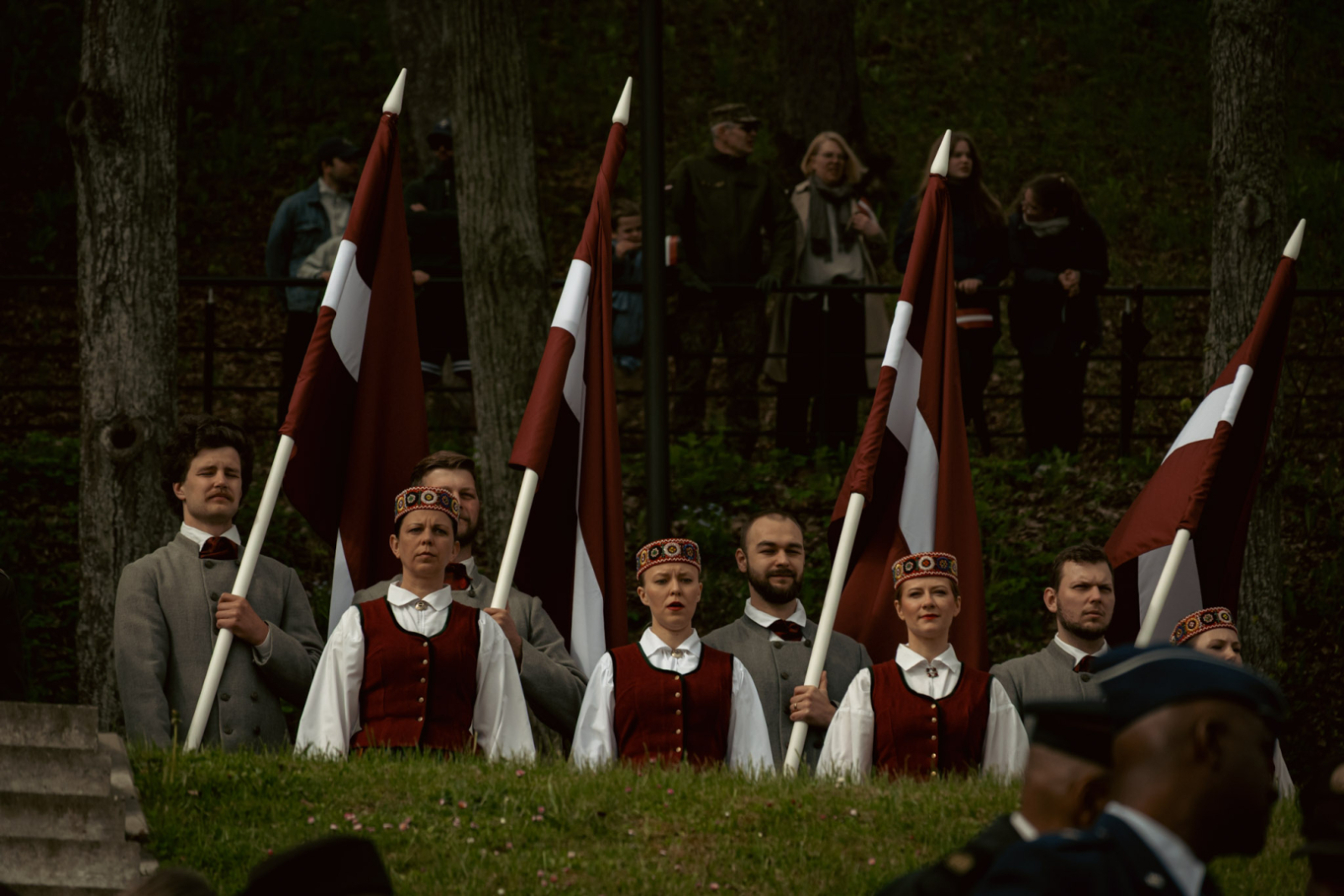 Cilvēki tautas tērpos tur rokās Latvijas karogus