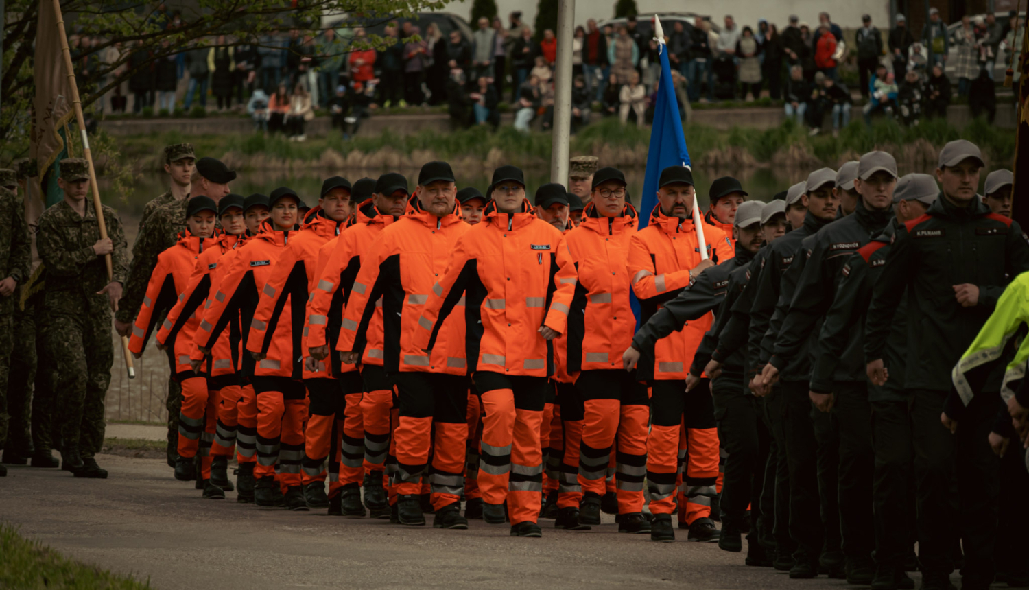 NMPD darbinieki oranžās formās soļo militārajā parādē