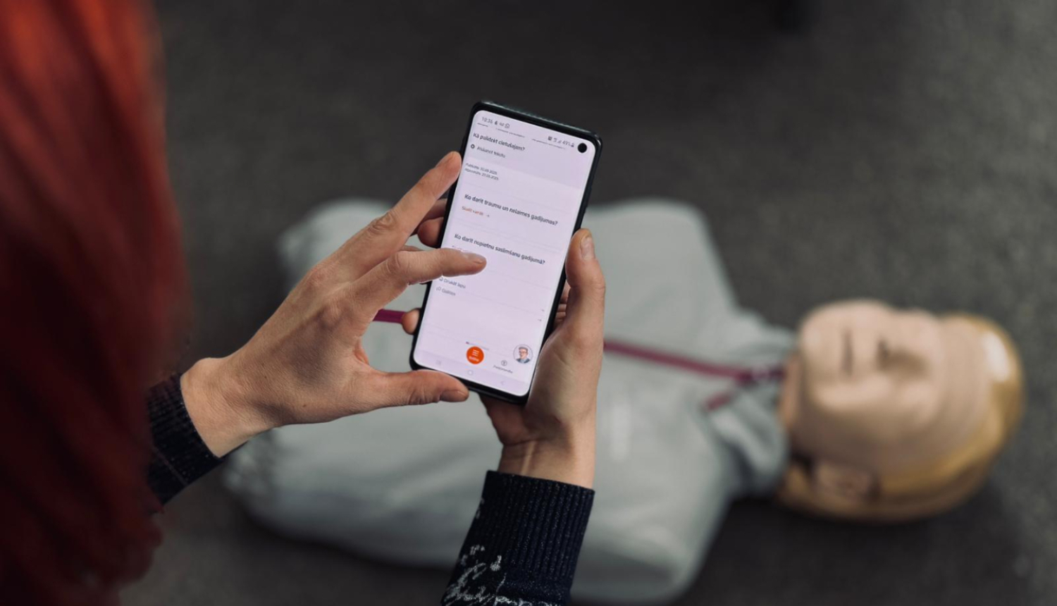 Sieviete rokās tur telefonu un uz grīdas redzams manekens