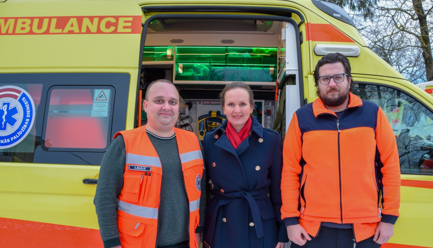 Veselības ministre vizītes laikā NMPD stāv pie operatīvā medicīniskā auto kopā ar diviem mediķiem