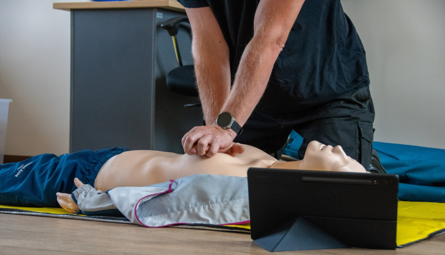 uz manekena sniedz atdzīvināšanas pasākumus. Manekenam blakus stāv planšetdators