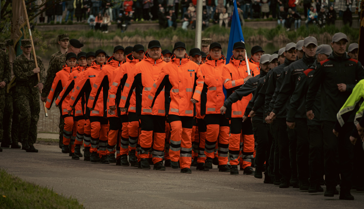 NMPD darbinieki oranžās formās soļo militārajā parādē