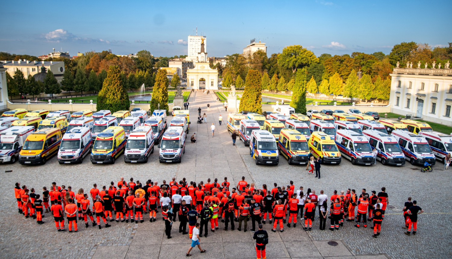 Skats no augšas, kur redzamas daudz dažādu ārvalstu ambulances un priekšā stāv daudz mediķu un paramediķu oranžās formās