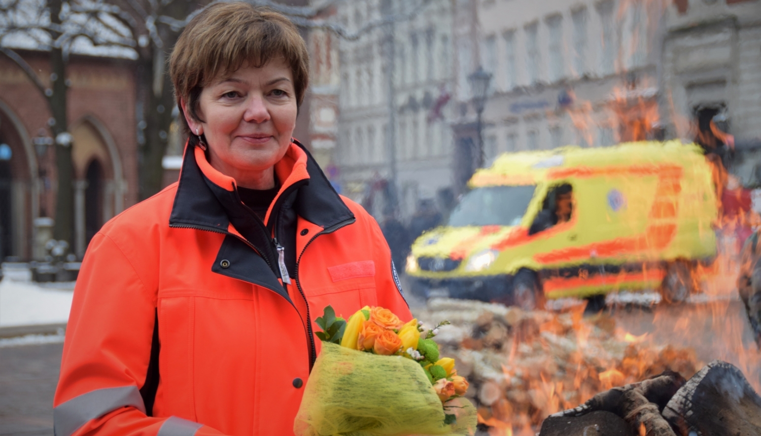 Dr. Dzintra Jakubaņeca stāv NMPD formā un fonā redzams operatīvais auto un ugunskurs