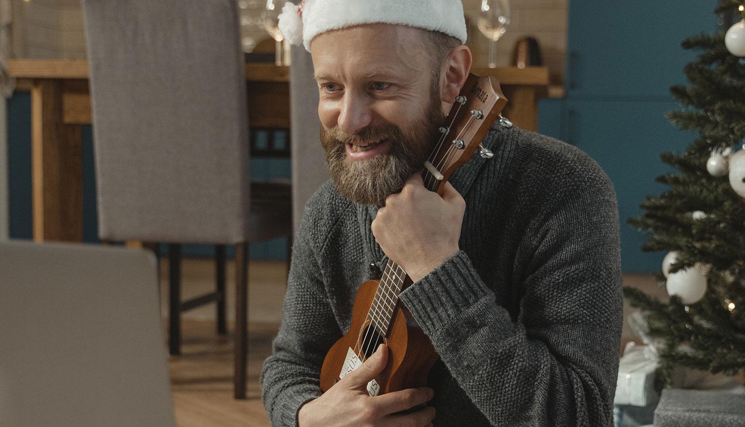 Vīrietis ar rūķu cepuri galvā spēlē ukuleli 