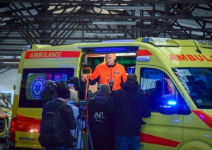 JaunaisNMPD operatīvais auto ar ieslēgtām bākugunīm. Auto iekšpusē stāv NMPD šoferis un stāsta medijiem par aprīkojumu